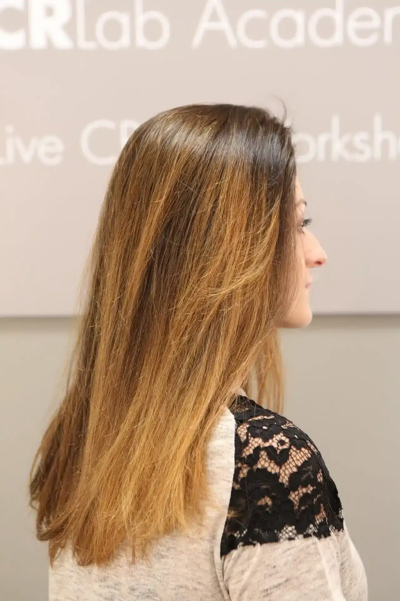 Woman with straight, ombre hair, wearing lace-trimmed top, side profile in a studio setting.
