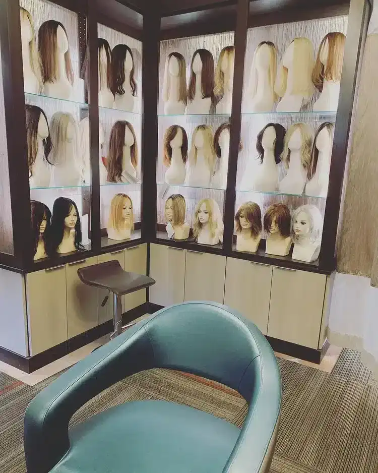 Wig display in a salon with various styles on mannequin heads, chair in foreground.