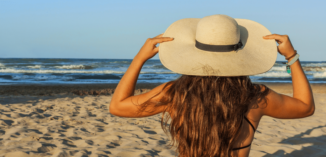 Young woman from behind, long hair, wearing summer hat in the beach. Rear view.